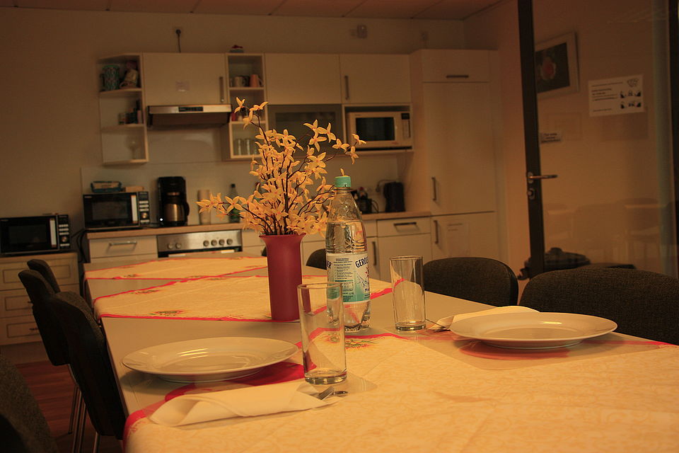 BW Tisch Ein gedeckter Tisch mit einer roten Vase im Innenbereich. Im Hintergrund ist eine Küche.