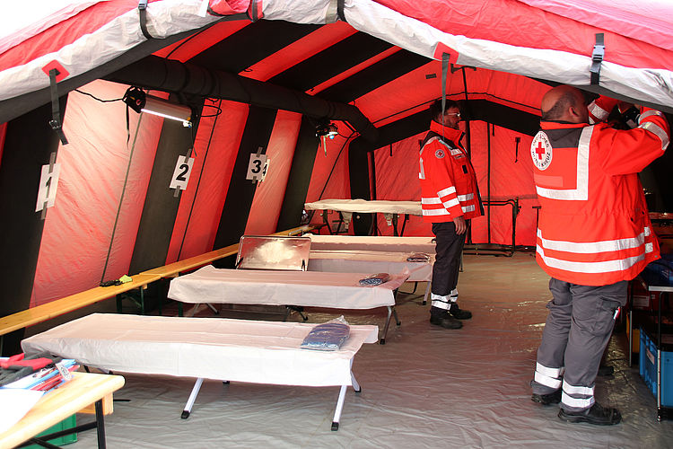Bad-Soden content img Innenansicht eines großen roten Sanitätszeltes mit mehreren Liegen und zwei Männern in DRK Kleidung.
