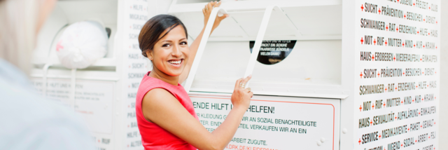 Kleidercontainer Stage Image Eine Dame steht vor einem DRK-Kleidercontainer und schaut lächelnd in die Kamera.