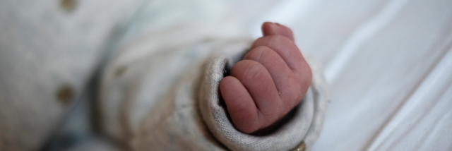 EH Säugling Stage Die Faust eines Säuglings liegt auf einem weißen Bett. Der Rest des Körpers ist aus dem Bild abgeschnitten.