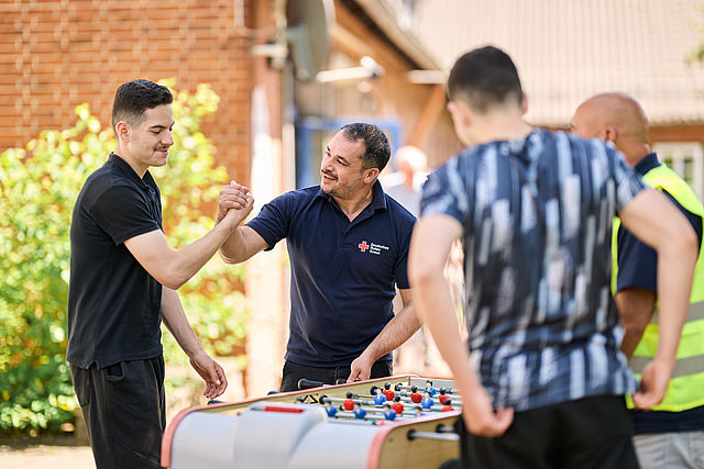 BFD_Content_Image Ein DRK Mitarbeiter und ein Jugendlicher schlagen vor einem Tischkicker die Hände ein.