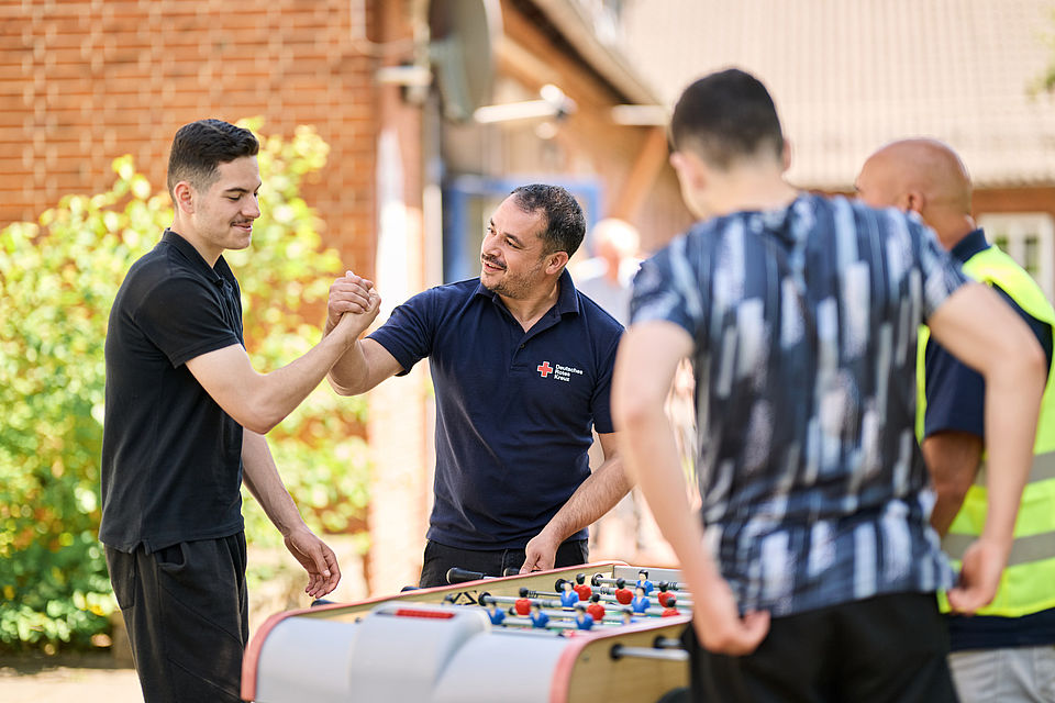 BFD_Content_Image Ein DRK Mitarbeiter und ein Jugendlicher schlagen vor einem Tischkicker die Hände ein.