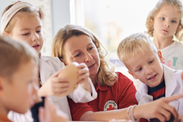 BetrieblicheEH_FortbildungBildungseinrichtungen Mitarbeiterin des DRK zeigt einer Gruppe Kinder die menschlichen Organe am Beispiel eines Torsos. Die Kinder schauen neugierig zu.