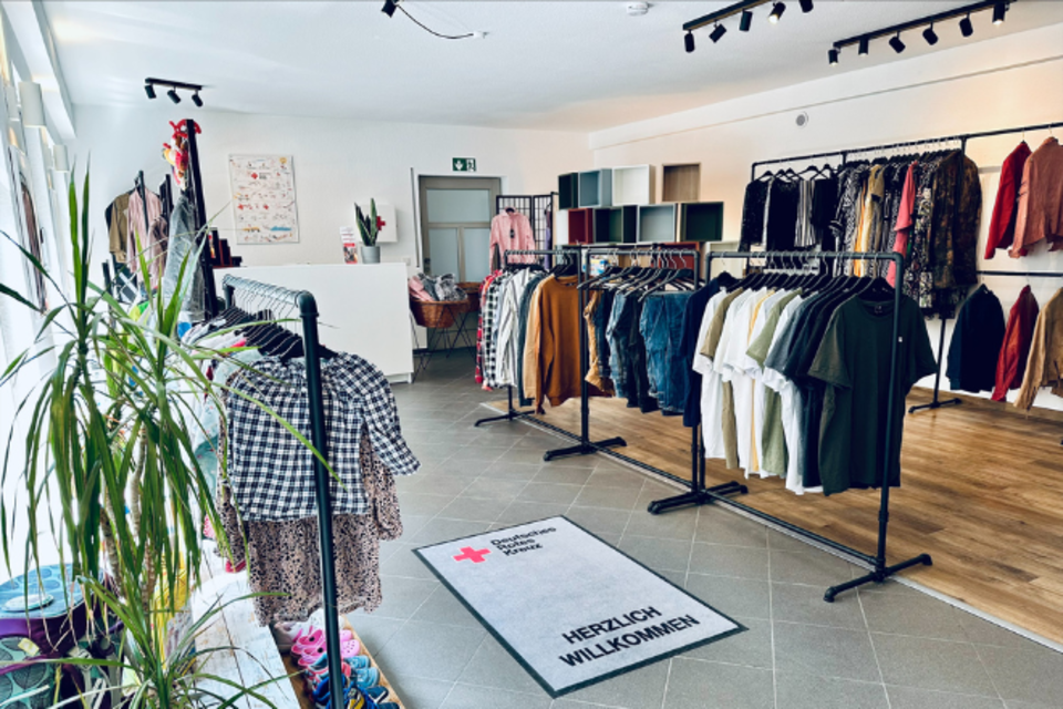 Kleiderladen Hochheim Innen 2 Innenbereich vom VielfachSchön in Hochheim. Die Kleiderstangen stehen in einem ordentlichen, hellen Raum, in dem eine Pflanze steht.