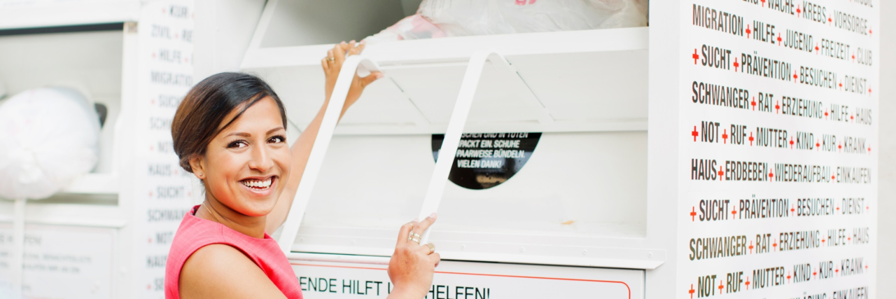 Sachspenden stage img Eine Frau öffnet lachend die Klappe eines Altkleidercontainers.