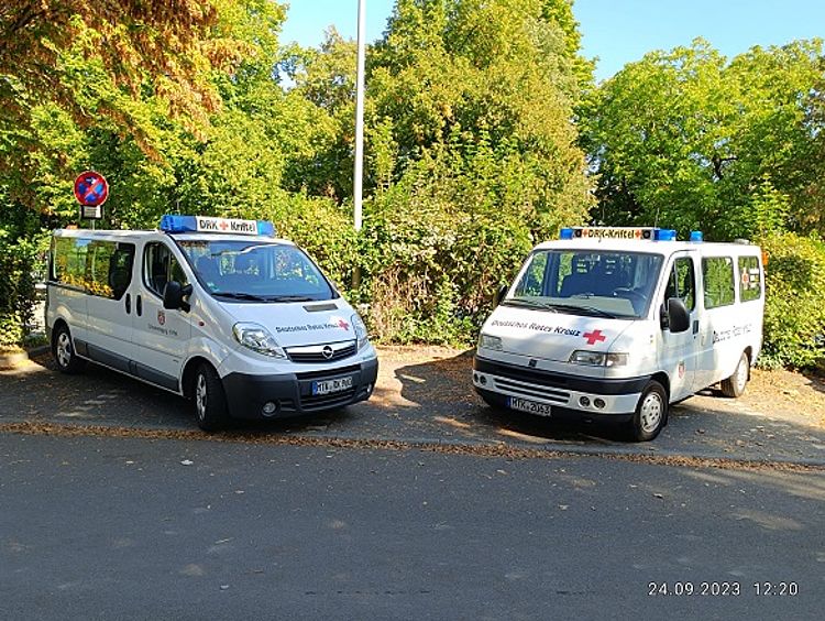 Kriftel content img Zwei Einsatzfahrzeuge stehen im Freien vor einem grünen Busch, der von der Sonne beleuchtet wird.