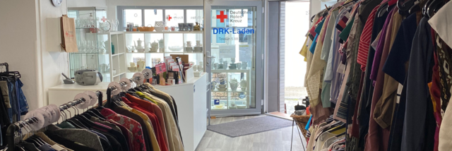 Kleiderladen Eppstein Stage Image Innenansicht des VielfachSchön in Eppstein: Blick durch einen Durchgang, umgeben von Kleiderstangen, hin zum dekorativen Schaufenster und dem Eingangsbereich.