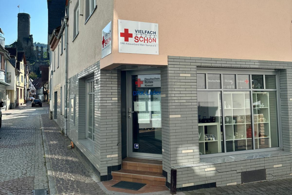 Kleiderladen Eppstein Außenansicht vom VielfachSchön in Eppstein. Die Tür ist an der Hausecke mit einem DRK-Logo des Ladens über dem Eingang. Die großen Fenster des Ladens sind mit Dekoration gefüllt.