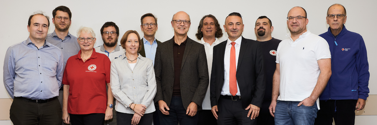 Kreisvorstand 12 Personen des Kreisvorstandes des DRK Main-Taunus e.V. stehen gemeinsam lächelnd vor einer weißen Wand.