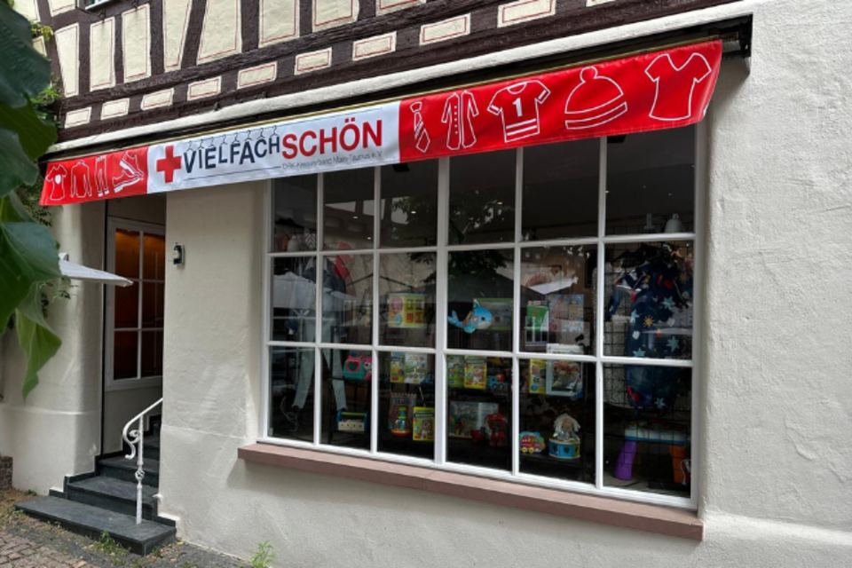 Kleiderladen Hofheim Außen Außenansicht vom VielfachSchön Hofheim: großes Schaufenster mit einer Markise im DRK-Design.