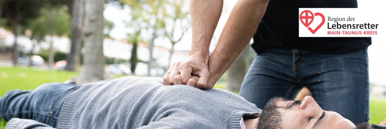 EH_Lebensretter_Stageimage Nahaufnahme einer Reanimation. Ein Mann im grauen Pulli liegt am Boden, in der Mitte auf seinem Brustkorb sind zwei verschränkte Hände einer anderen Person, die eine Herzdruckmassage durchführt.